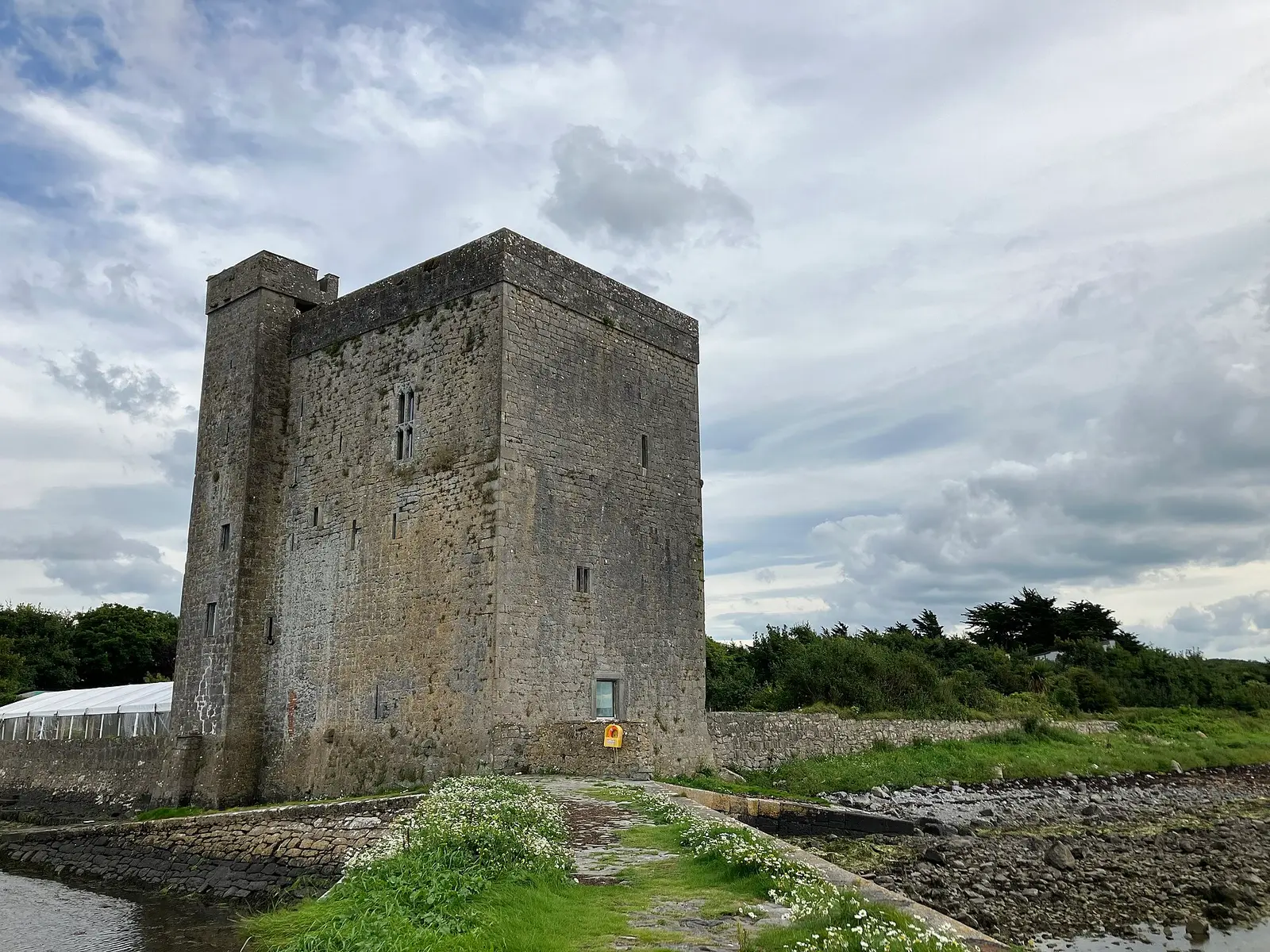 Oranmore Castle, a rectangular tower house by the sea, during low tide, under a cloudy sky.